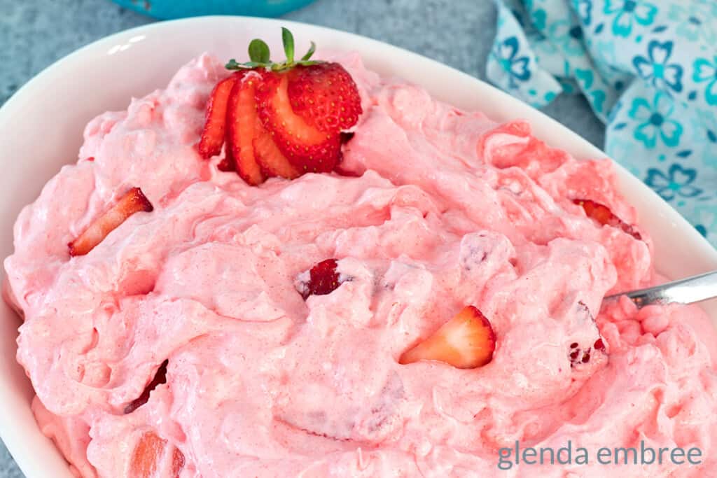Pink Strawberry Cottage Cheese Salad in a white oval bowl. There is a sliced strawberry garnish at one end of the bowl.  Easy recipe.