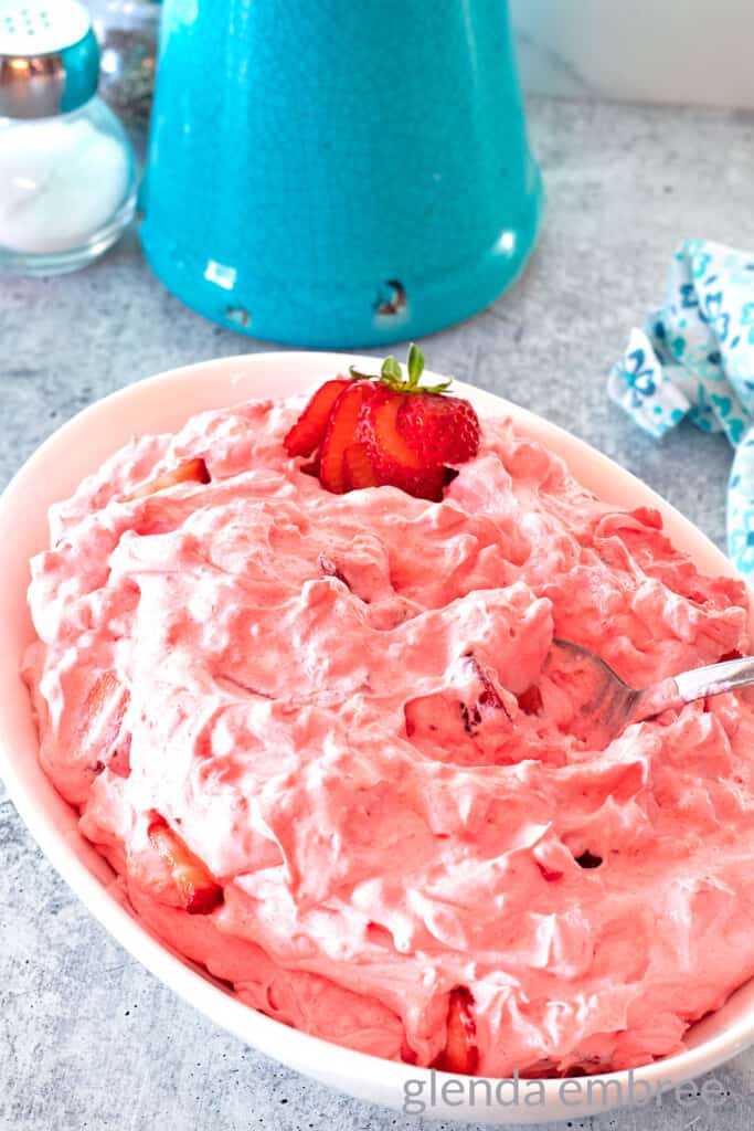 Pink Strawberry Cottage Cheese Salad in a white oval bowl. There is a sliced strawberry garnish at one end of the bowl.