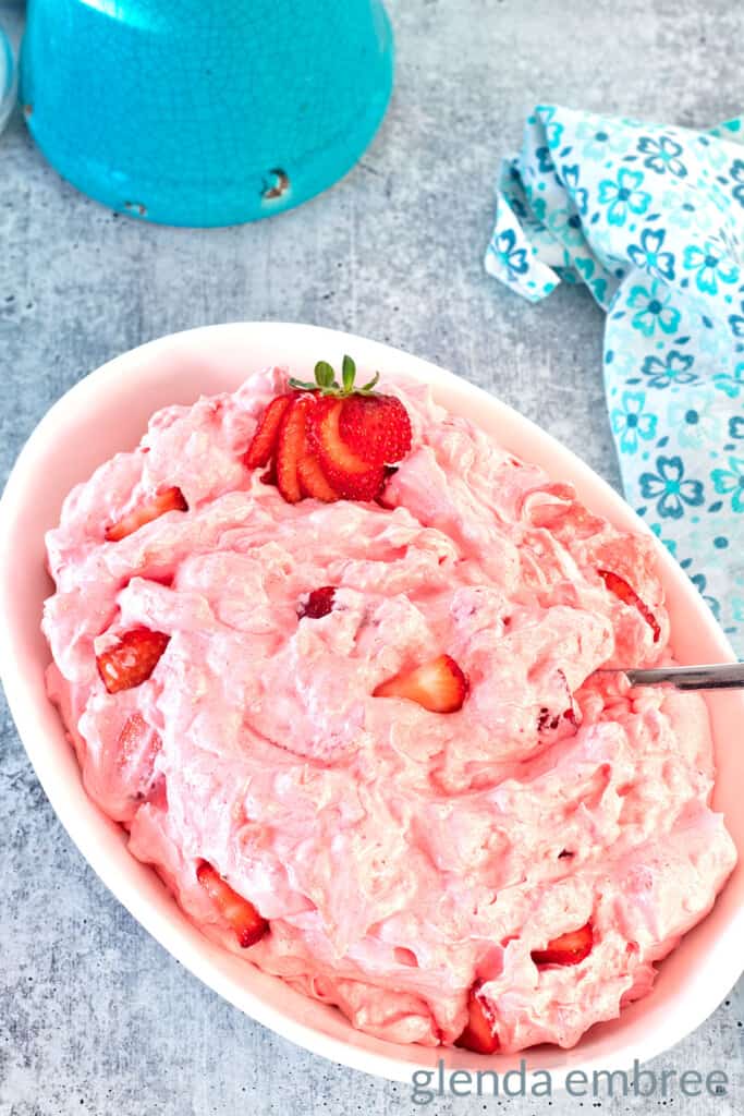 Pink Strawberry Cottage Cheese Salad in a white oval bowl. There is a sliced strawberry garnish at one end of the bowl.