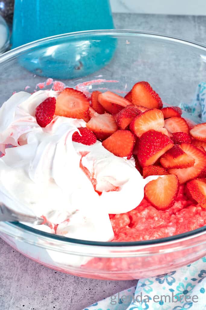 cottage cheese, strawberry gelatin, cool whip and sliced fresh strawberries in a clear glass mixing bowl