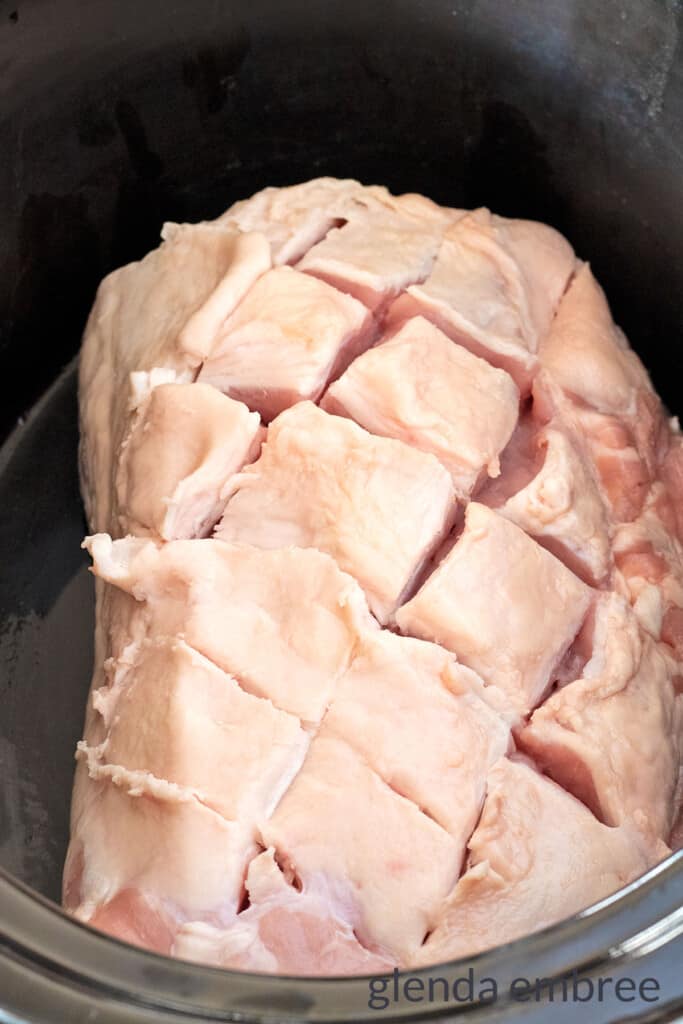 Raw pork loin in a slow cooker with crisscross pattern cut through the fat cap down to the meat