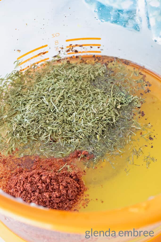 Ingredients for Shirazi Salad dressing in a liquid measuring cup: olive oil, lemon juice, dried dill, sumac, salt and pepper.