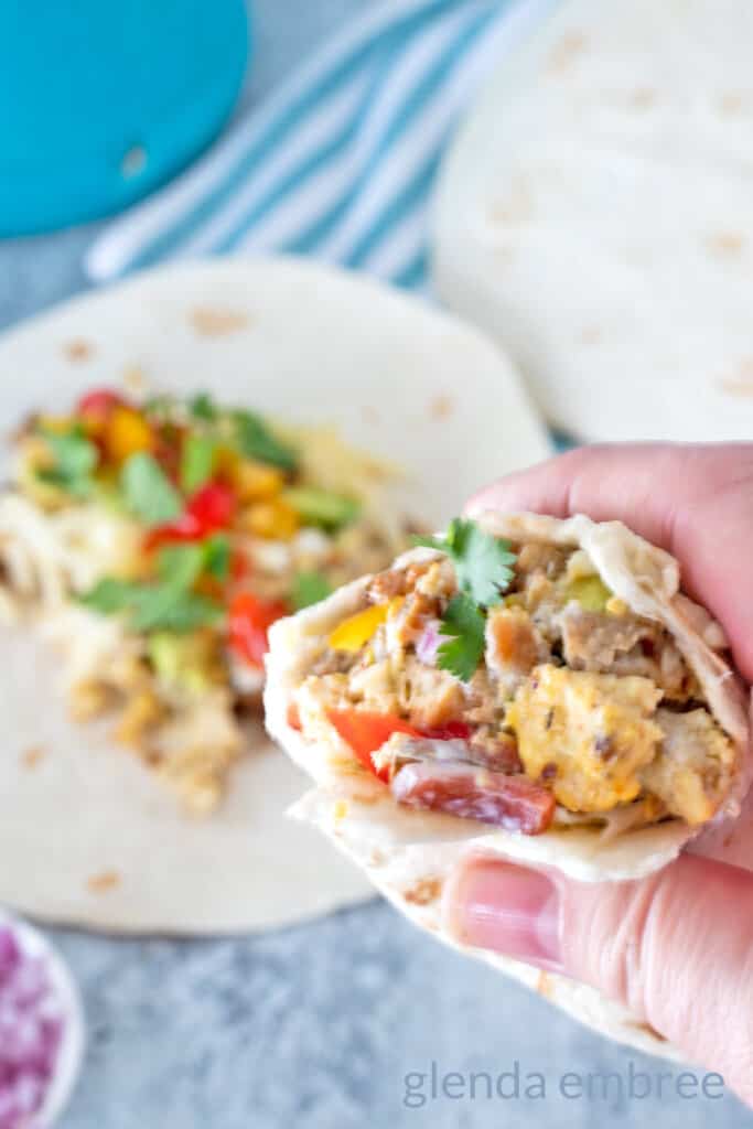Breakfast taco with bites out held in a hand with unrolled taco in background