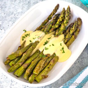 Air Fryer Asparagus drizzled in Hollandaise in a white oval serving dish.