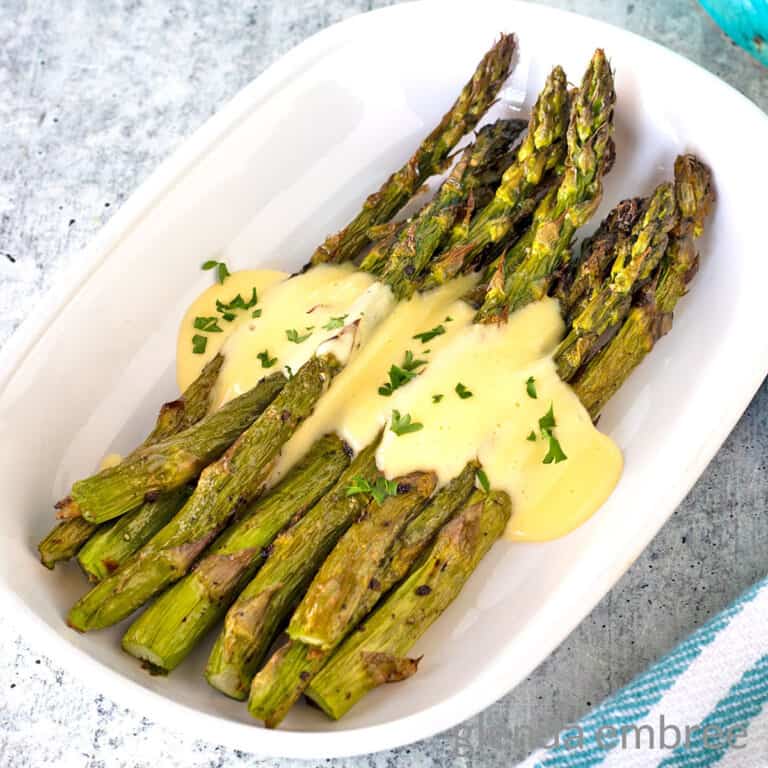 Air Fryer Asparagus drizzled in Hollandaise in a white oval serving dish.