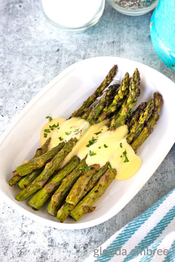 Air Fryer Asparagus drizzled in Hollandaise in a white oval serving dish.