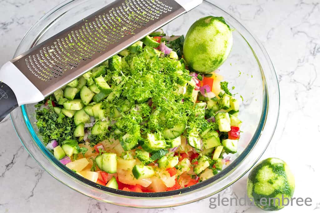 Clear glass mixing bowl with pineapple salsa ingredients.