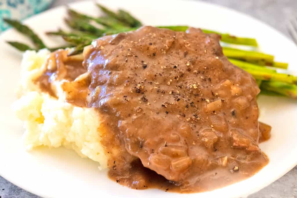 Crock Pot Cube Steak on a white plate with mashed potatoes and asparagus.
