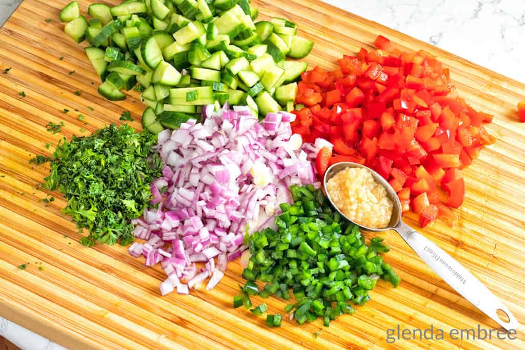 Cucumbers, red bell pepper, poblano pepper, red onion and parsley on a wedding cutting board, chopped and ready to make pineapple salsa 
