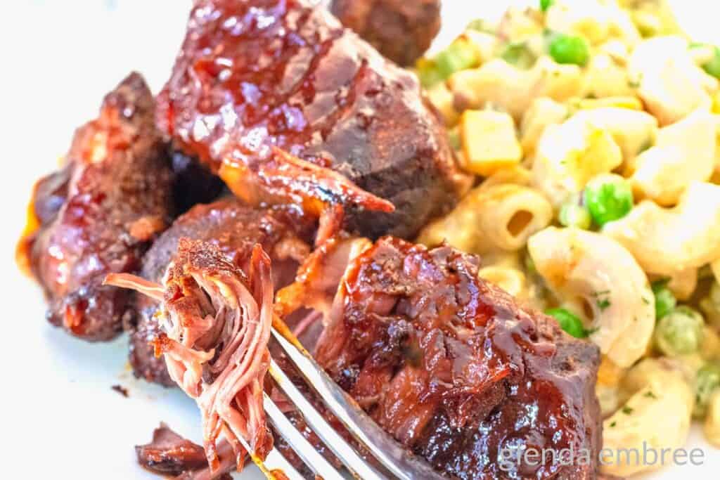 Country Style Ribs- Slow Cooker Country Ribs on a white plate with macaroni salad and a fork taking a bite.