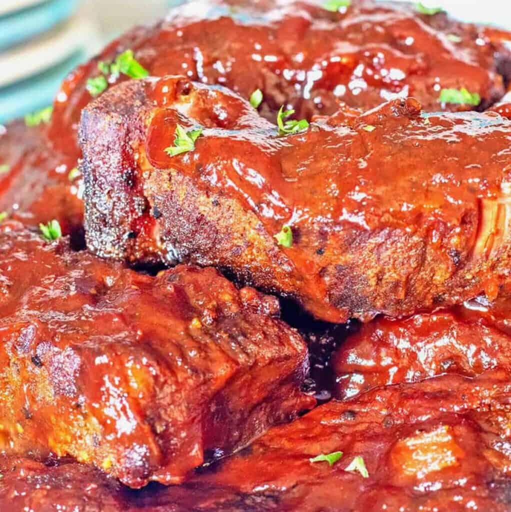 BBQ Slow Cooker Country Ribs stacked on a cream-colored stoneware platter.