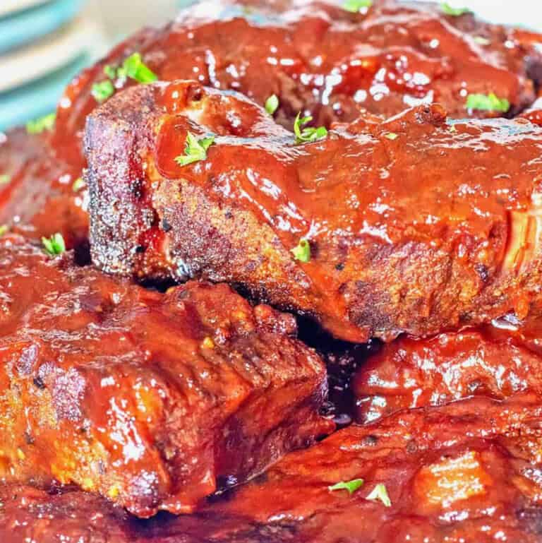 BBQ Slow Cooker Country Ribs stacked on a cream-colored stoneware platter.