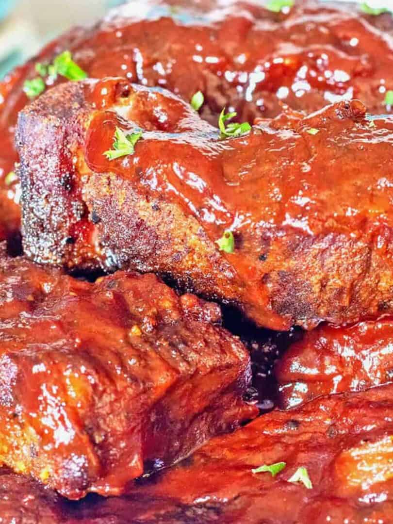 BBQ Slow Cooker Country Ribs stacked on a cream-colored stoneware platter.