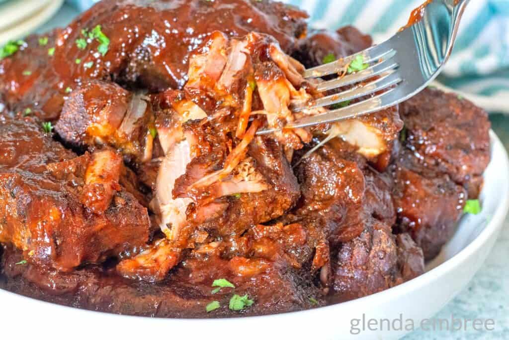Country Style Ribs - Slow Cooker Country Ribs in a white serving dish with a fork lifting a bite upwards.