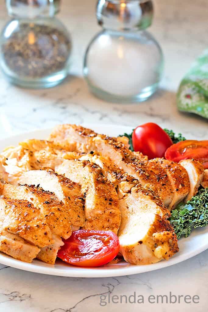 Perfect Baked Chicken Breasts on a white plate with kale and cherry tomatoes.  Great batch cooking recipe for creating intentional leftovers.