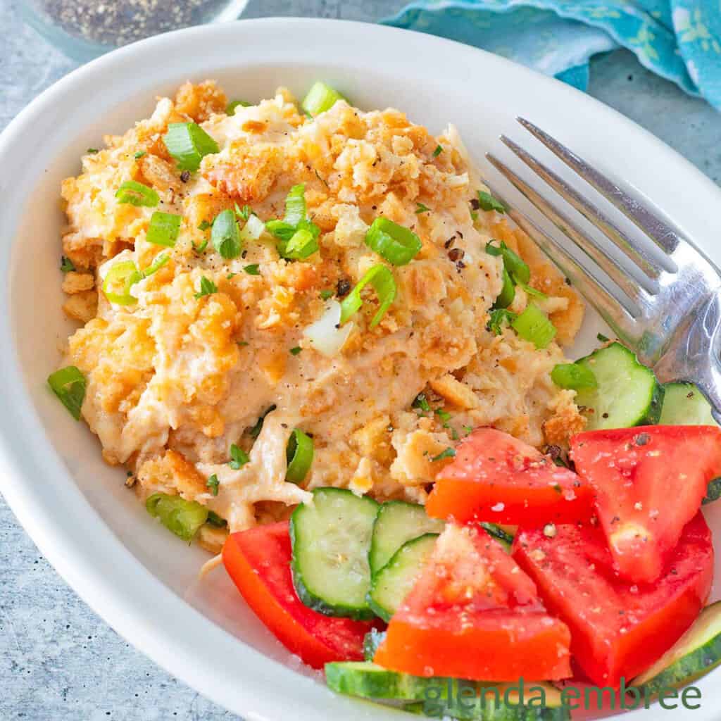 Million Dollar Chicken Casserole in a white dish with cucumber and tomato salad.