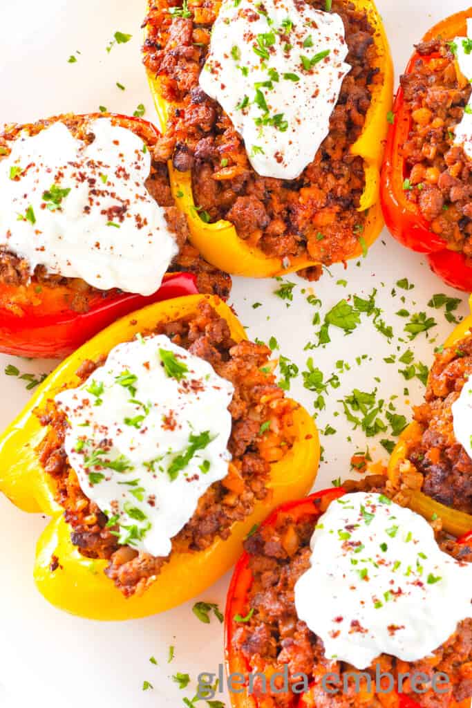 Air Fryer Stuffed Peppers with Curried Ground Lamb topped with Greek yogurt, cilantro and ground sumac sitting on a white plate.
