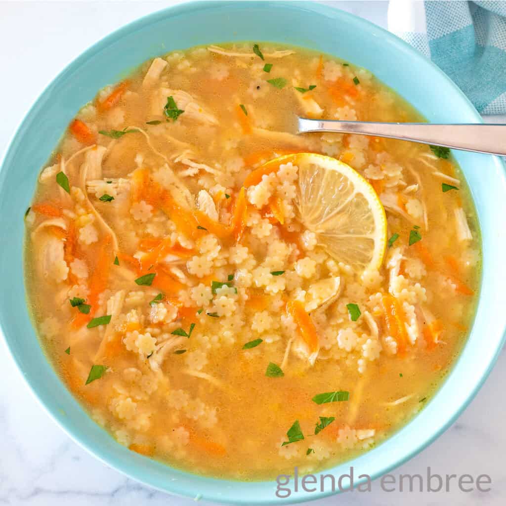 Chicken Pastina Soup (Chicken and Stars) in a blue ceramic bowl garnished with a slice of lemon.