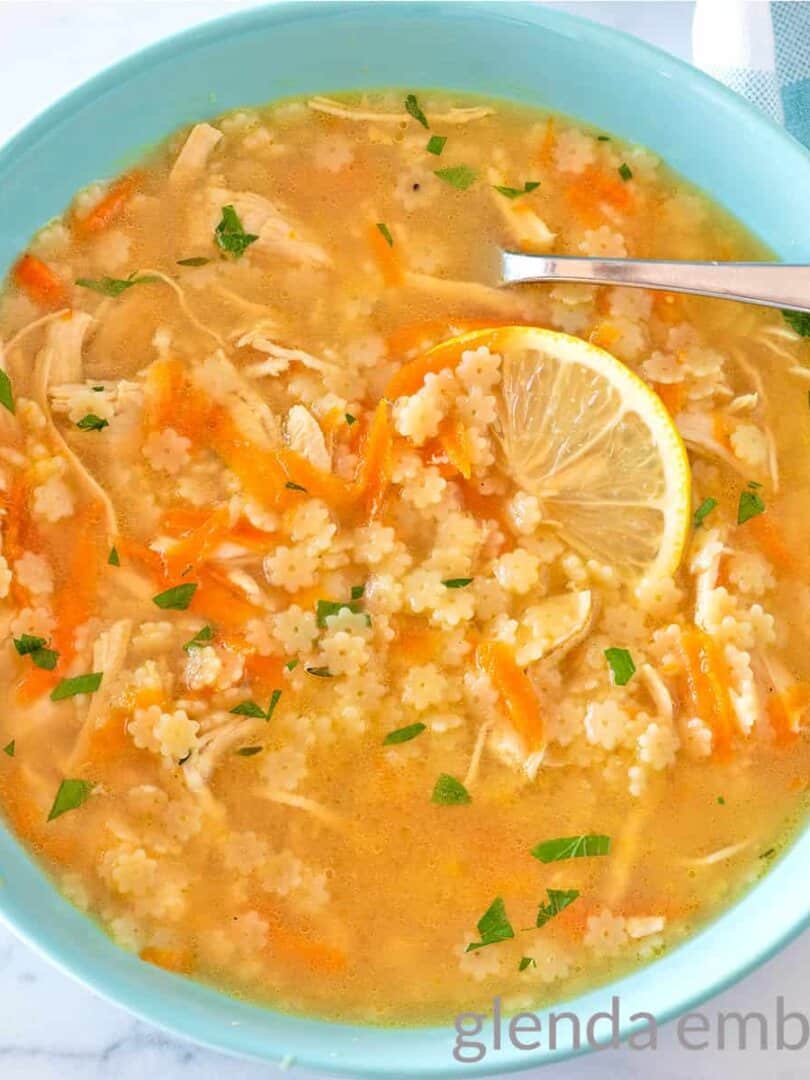 Chicken Pastina Soup (Chicken and Stars) in a blue ceramic bowl garnished with a slice of lemon.