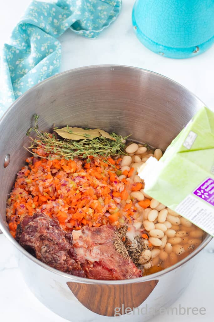 Adding broth to the stock pot with pork neck bones, beans, veggies and hebs.