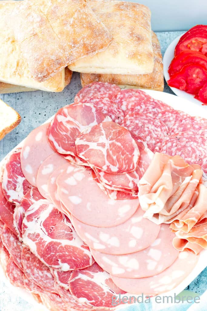 Italian meat selection on a white platter for making Italian grinder sandwiches.