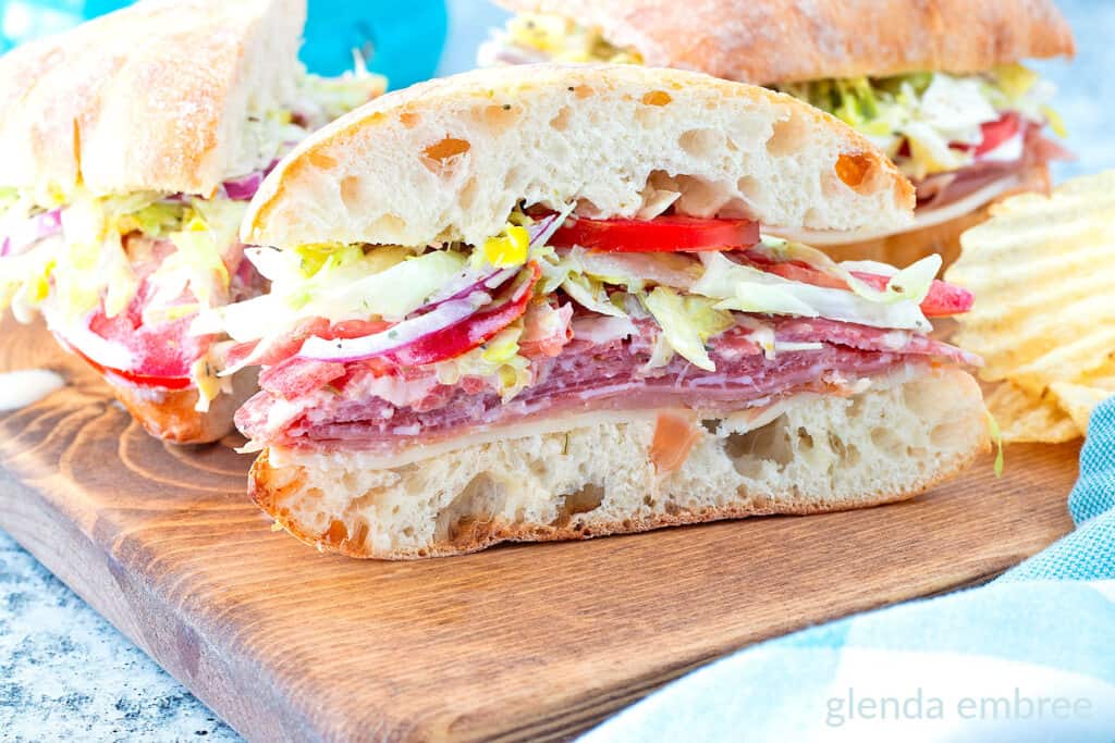 Italian Grinder Sandwich cut to see the contents and sitting on a wooden cutting board.