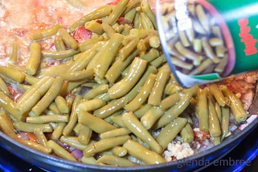 Adding canned green beans to the skillet.