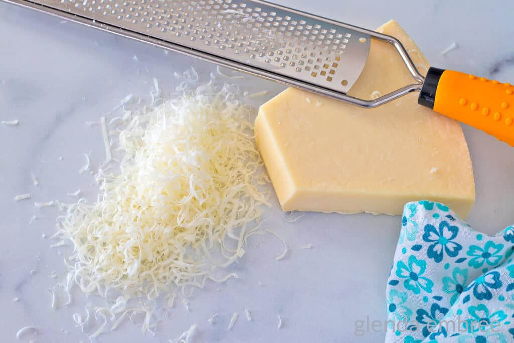 A block of Parmesan cheese next to a pile of finely grated cheese and a microplane grater.