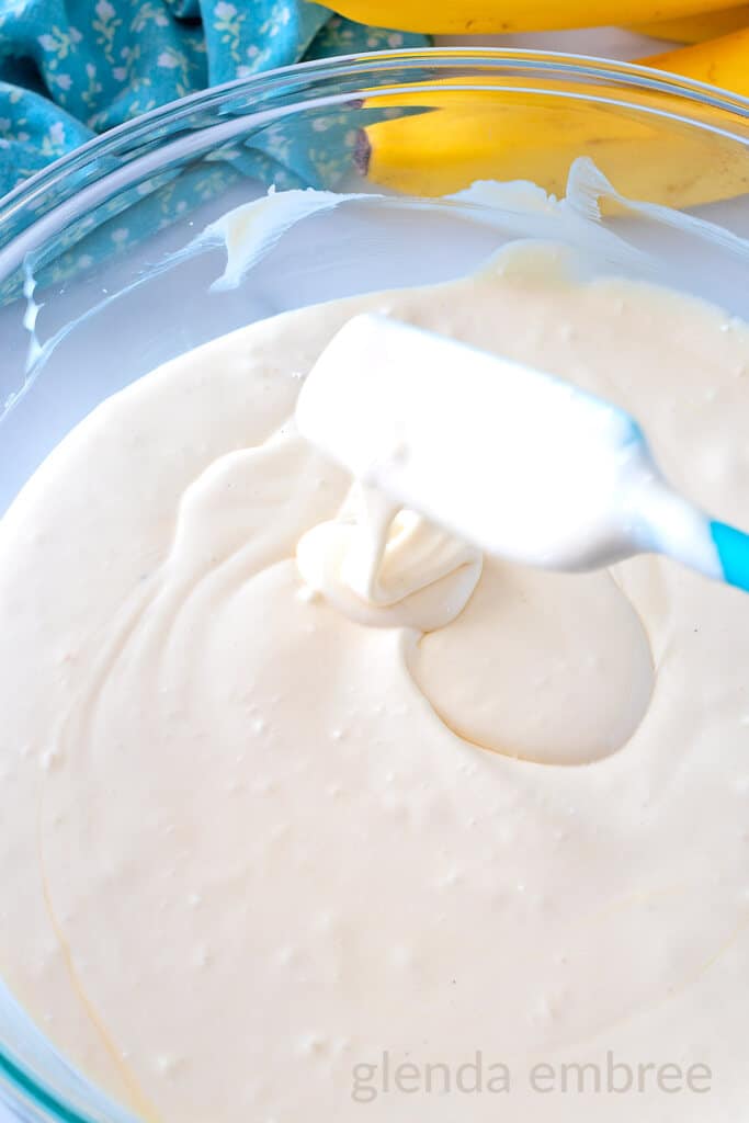 Spatula lifting pudding mixture out of clear glass bowl to demonstrate the consistency.