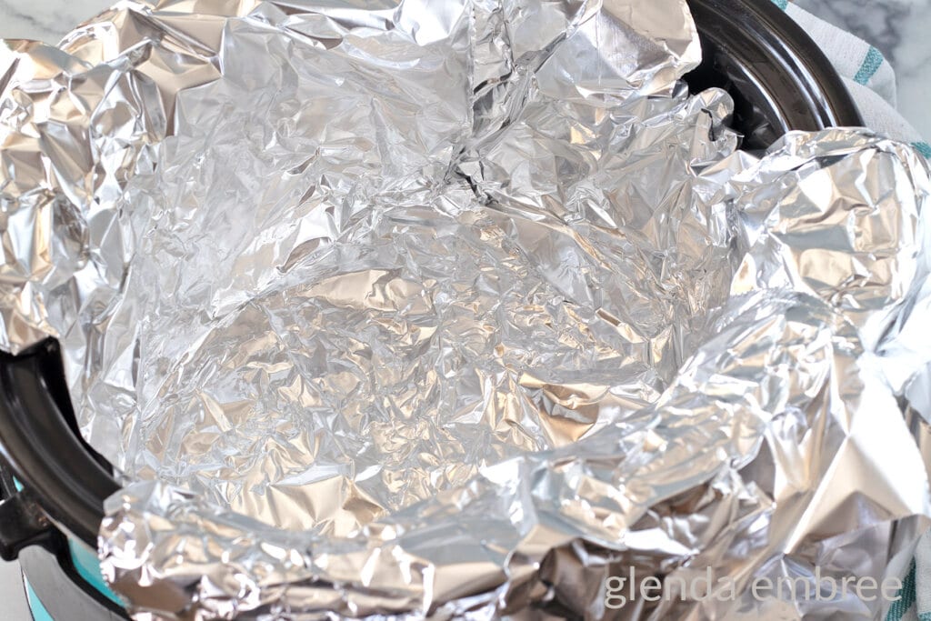Lining slow cooker with aluminum foil.