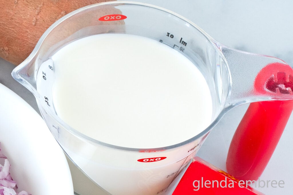 Whole milk in a clear liquid measuring cup with a red handle.