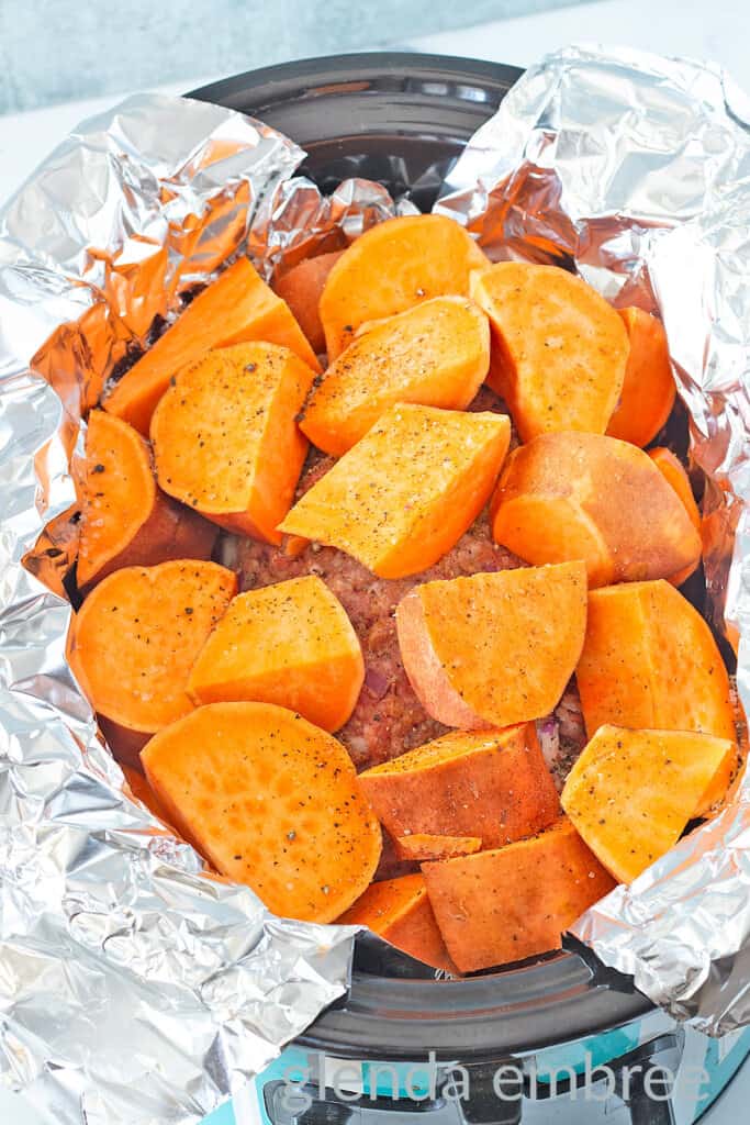 Sweet potatoes over a meatloaf in a foil-lined crock pot.
