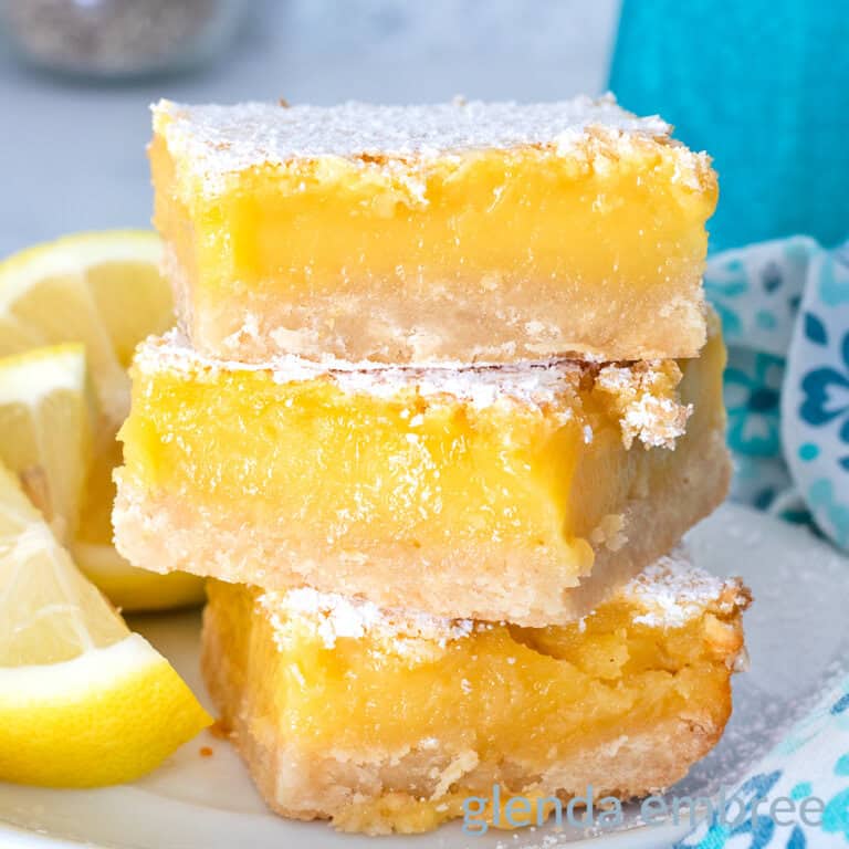 Lemon Bars on a white ceramic plate with lemon wedges.