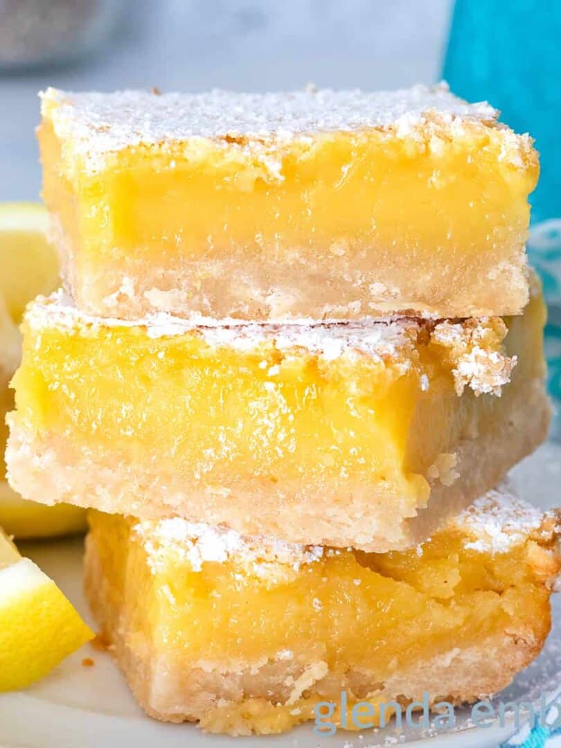 Lemon Bars on a white ceramic plate with lemon wedges.