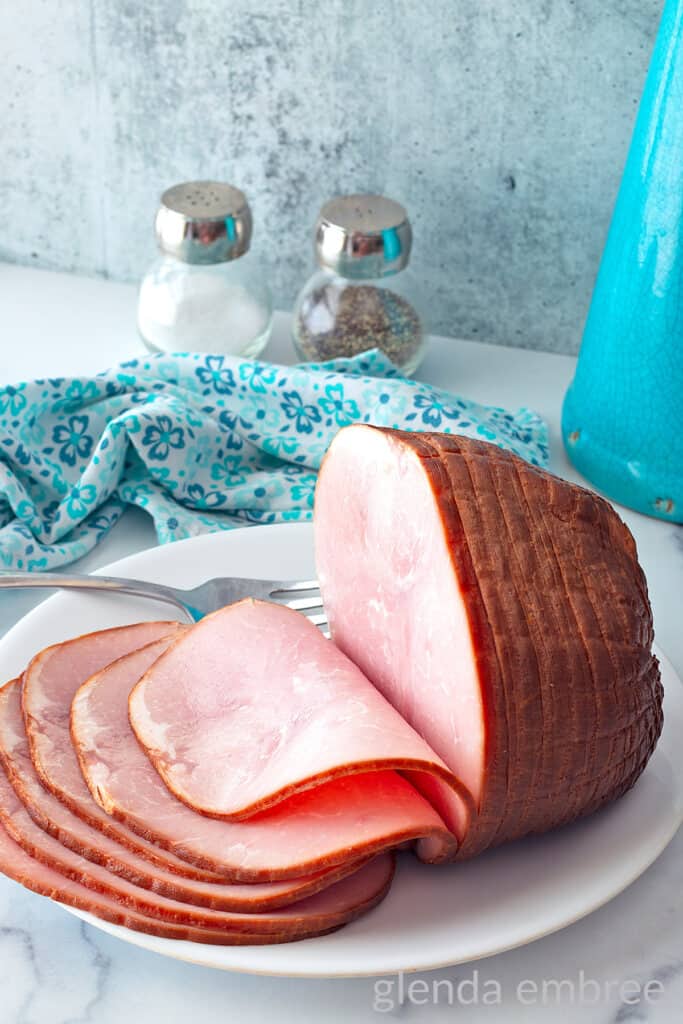 Baked ham sliced on a white platter.