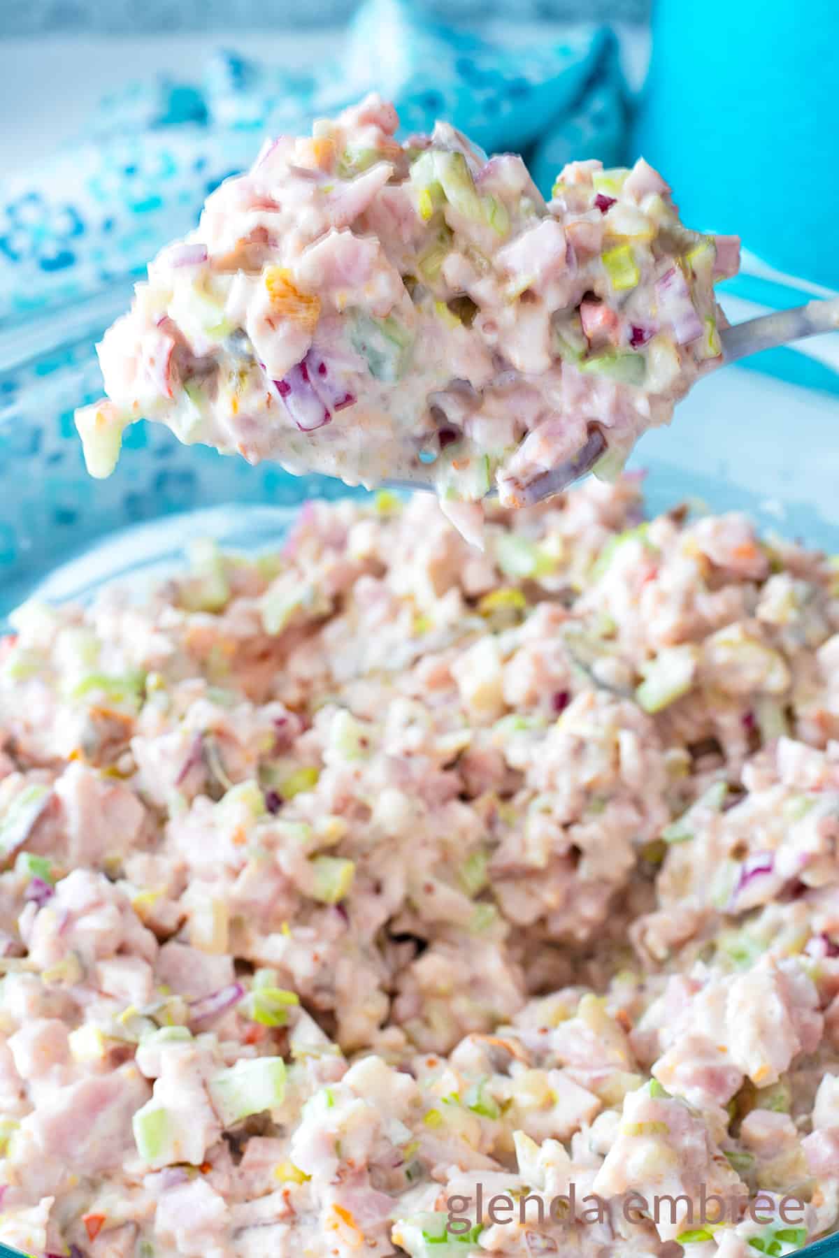 Old Fashioned ham Salad (Deviled Ham) lifted out of a clear glass mixing bowl on a fork.