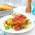 Impossible Taco Pie (Bisquick Taco Pie) topped with sour cream lettuce and tomatoes on a white plate.