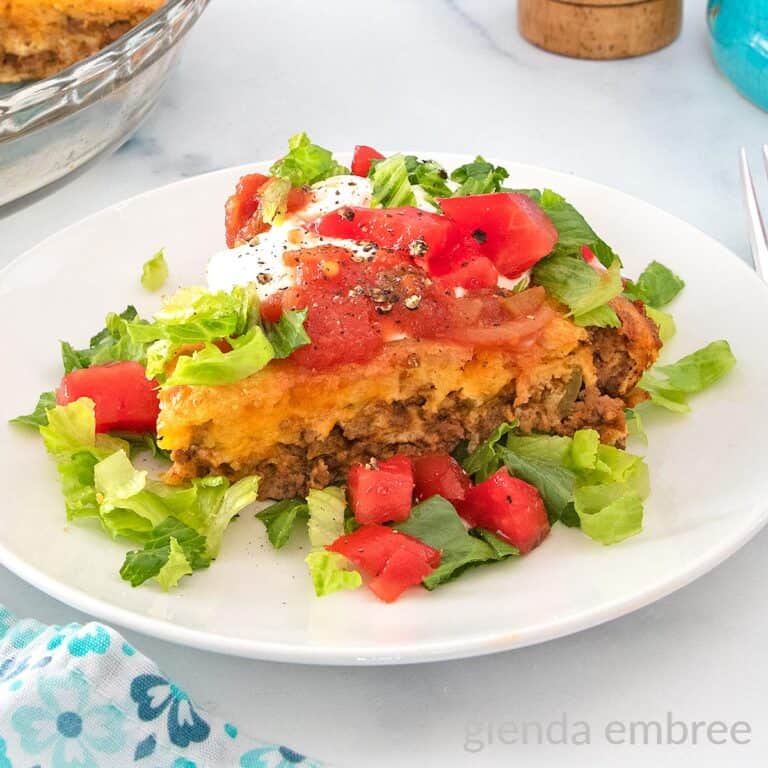 Impossible Taco Pie (Bisquick Taco Pie) topped with sour cream lettuce and tomatoes on a white plate.