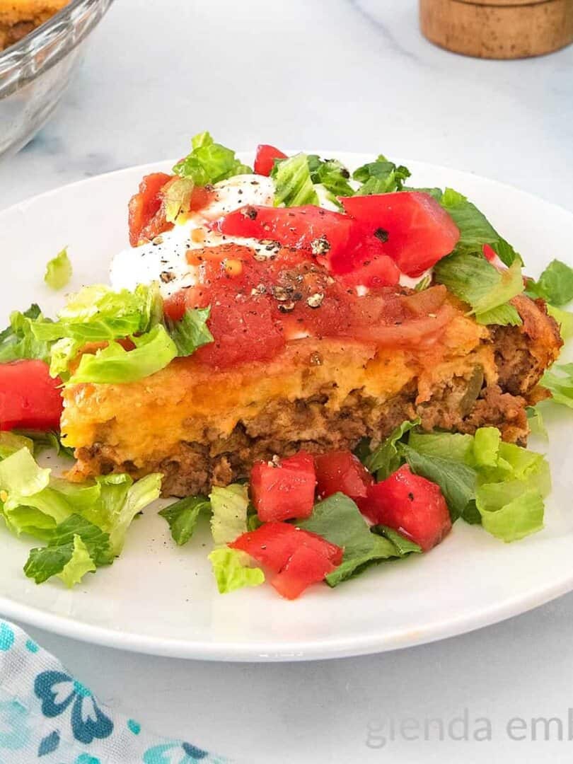 Impossible Taco Pie (Bisquick Taco Pie) topped with sour cream lettuce and tomatoes on a white plate.