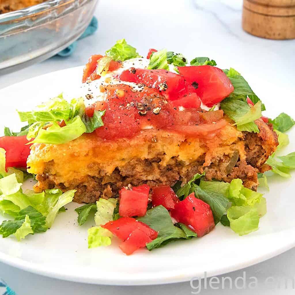 Impossible Taco Pie (Bisquick Taco Pie) topped with sour cream lettuce and tomatoes on a white plate.