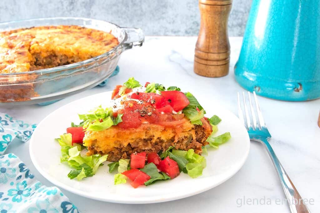 Impossible Taco Pie (Bisquick Taco Pie) topped with sour cream lettuce and tomatoes on a white plate.