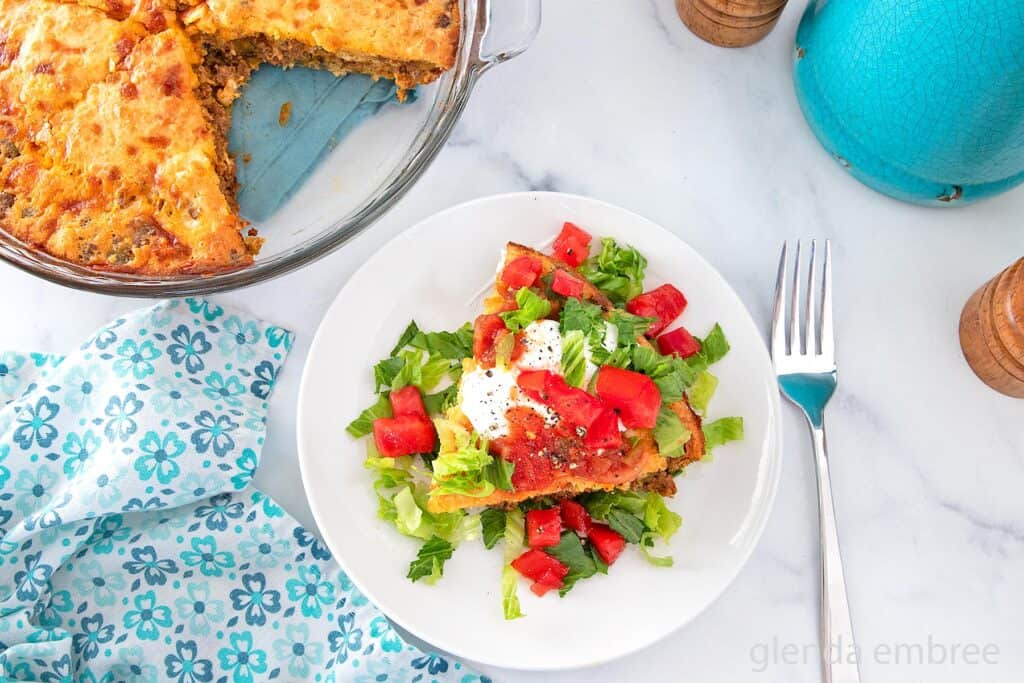 Impossible Taco Pie (Bisquick Taco Pie) topped with sour cream lettuce and tomatoes on a white plate.