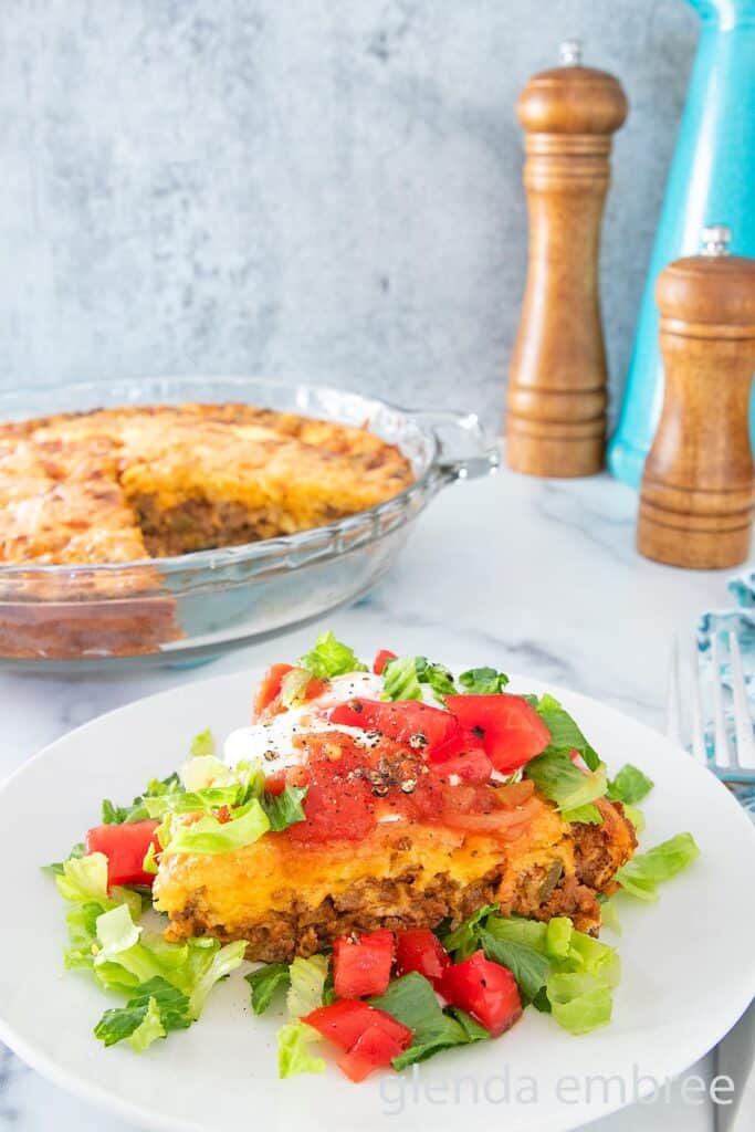 Impossible Taco Pie (Bisquick Taco Pie) topped with sour cream lettuce and tomatoes on a white plate.