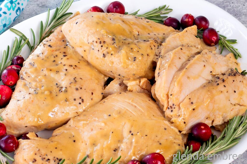 Crockpot Turkey Tenderloins on a white platter with fresh rosemary and cranberries for garnish.