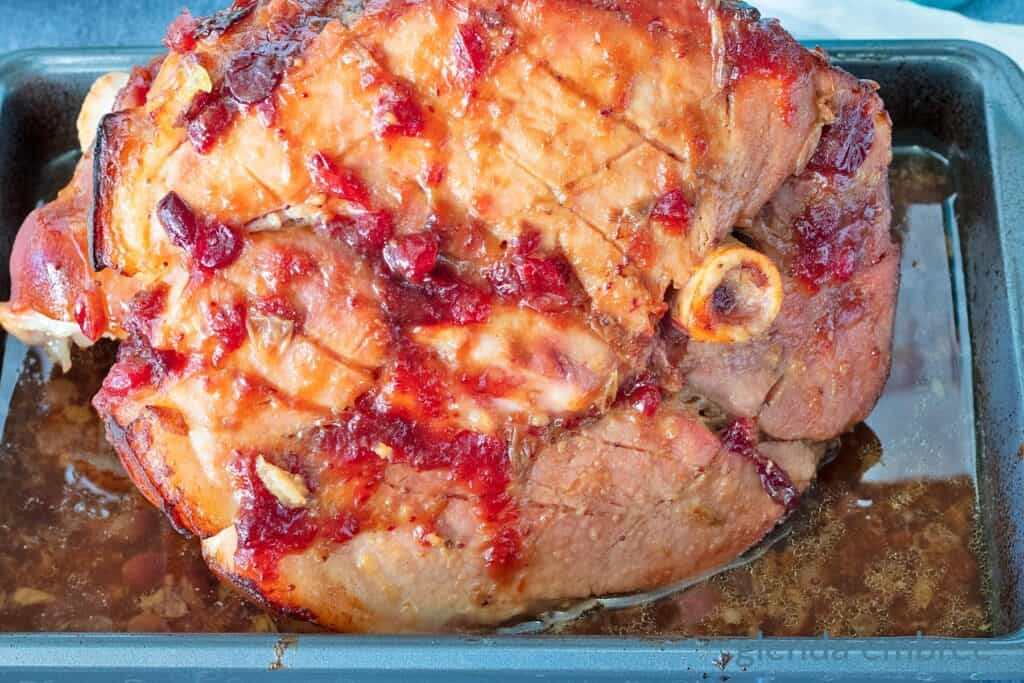 Fully-baked Cranberry Glazed Ham still resting in the roasting pan with the juices.