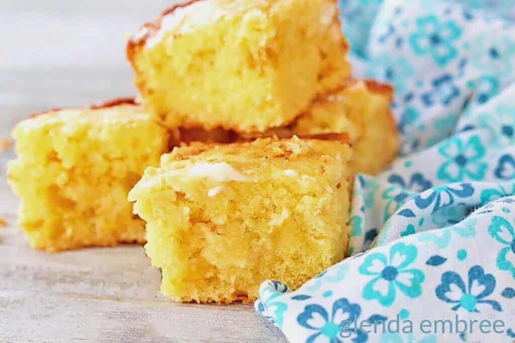 Sweet cornbread squares stacked on a wooden table next to a blue calico print cloth napkin.