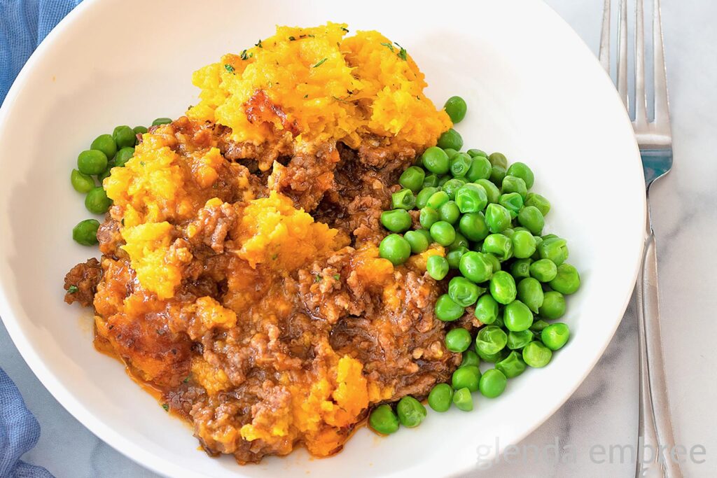 Cottage Pie (Shepherd's Pie) with Mashed Butternut Squash served in a white ceramic bowl with buttered green peas.