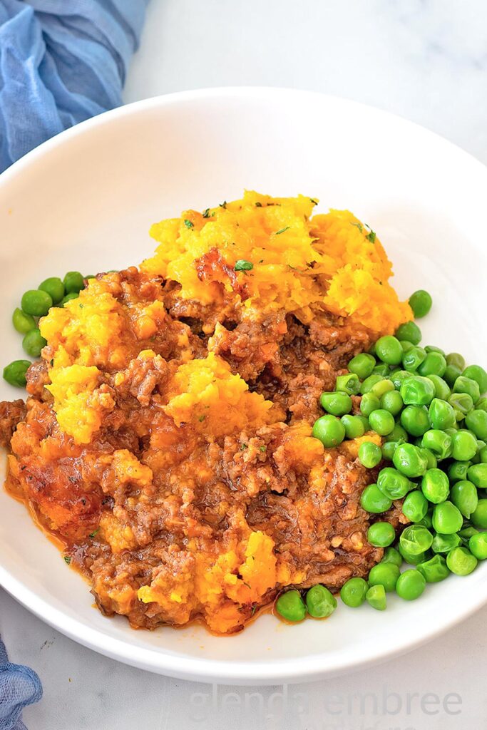 Cottage Pie (Shepherd's Pie) with Mashed Butternut Squash served in a white ceramic bowl with buttered green peas.