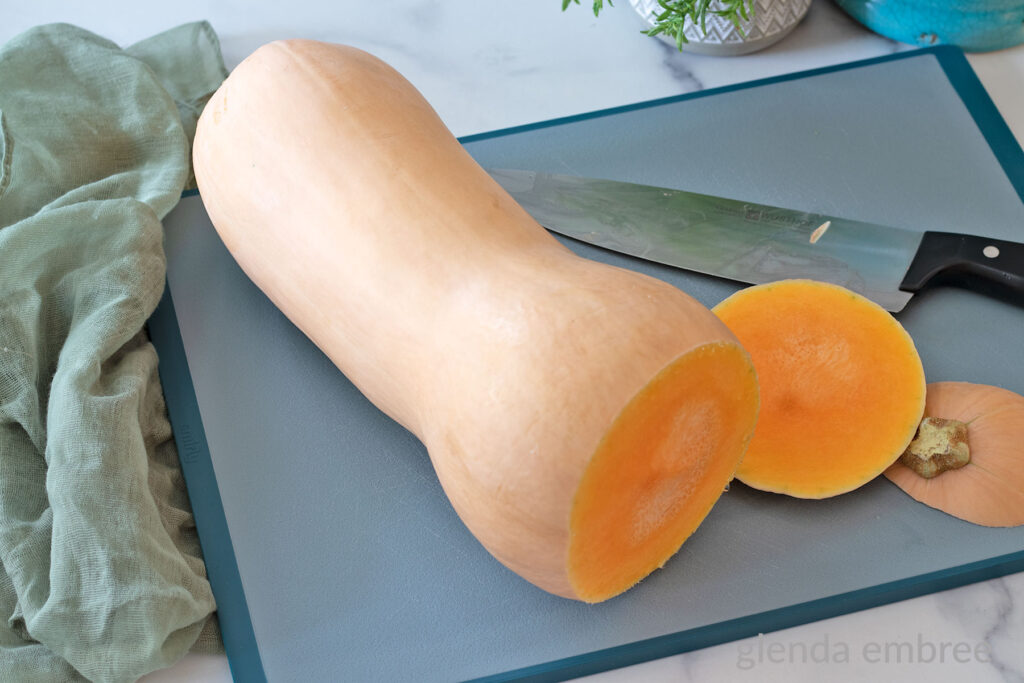 Whole butternut squash on a cutting board with the ends cut off.