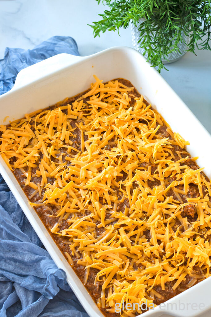 Cottage Pie Filling sprinkled with Cheddar cheese in a white ceramic baking dish.